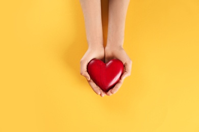 Woman holding decorative heart on color background, top view