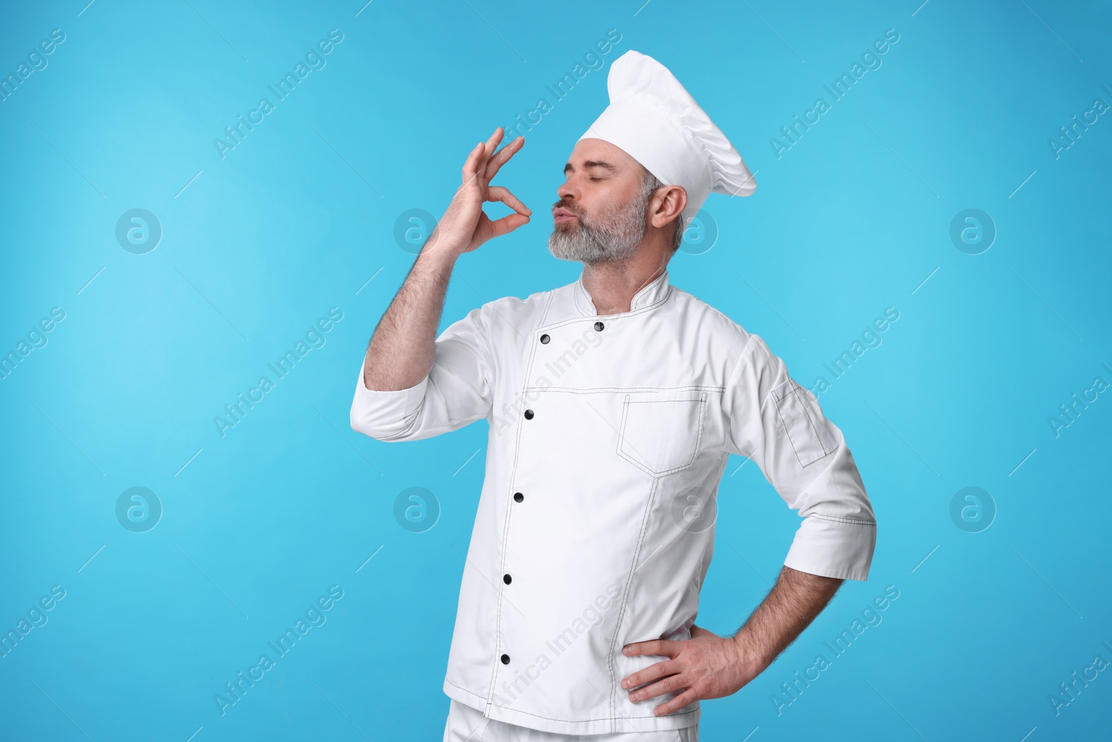 Photo of Chef in uniform showing perfect sign on light blue background