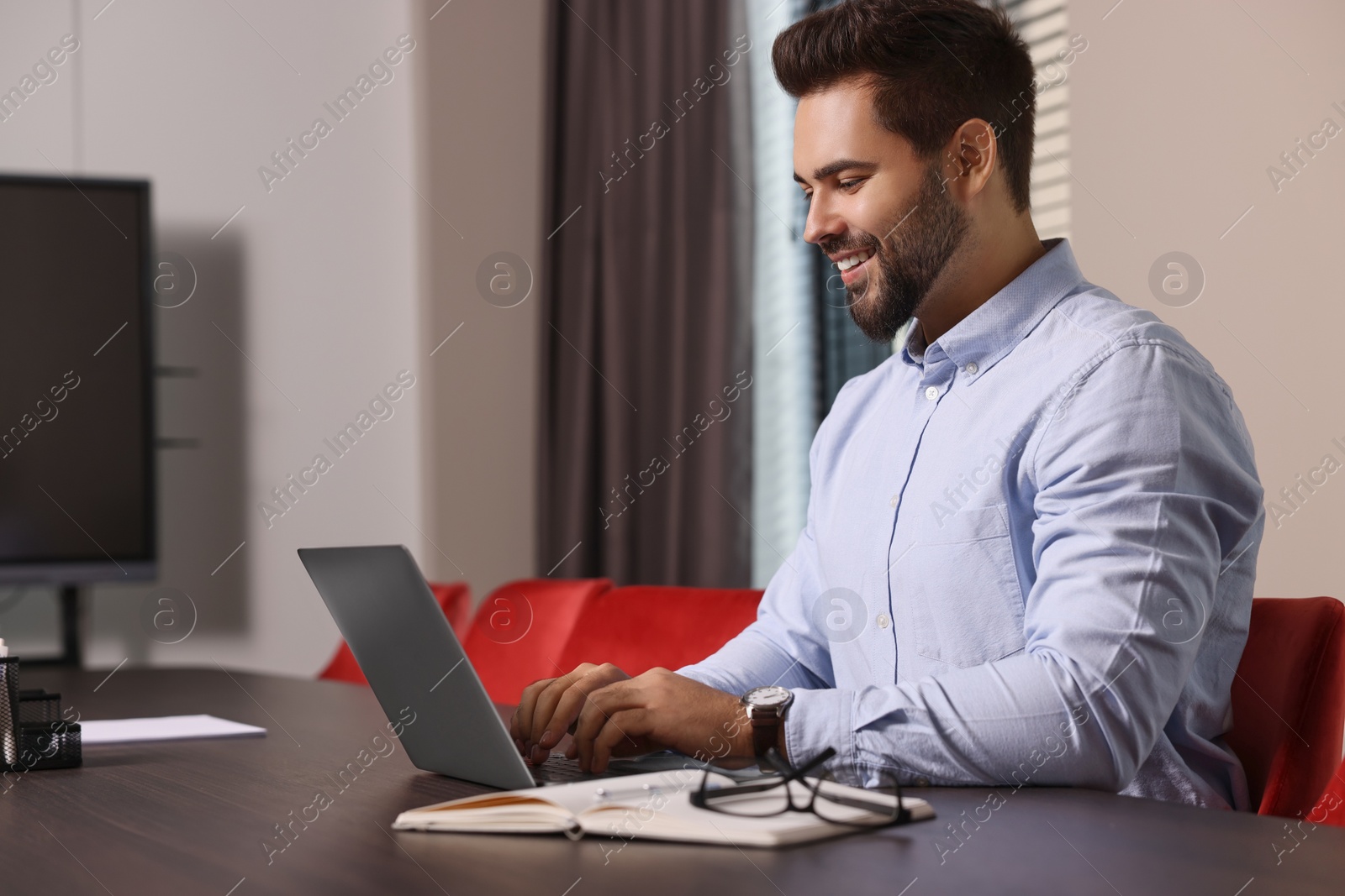 Photo of Happy young man working on laptop at table in office