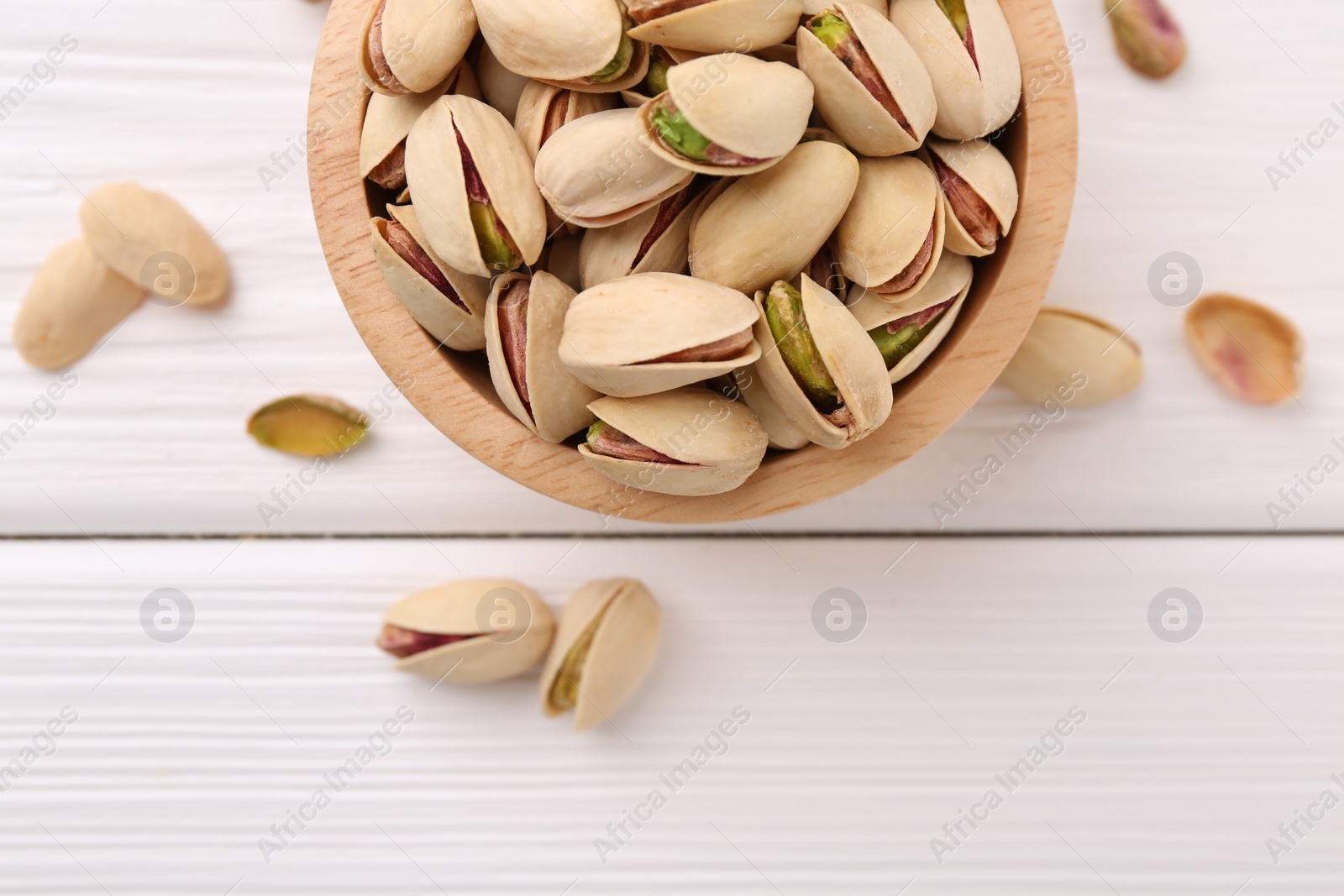Photo of Tasty pistachios in bowl on white wooden table, top view. Space for text