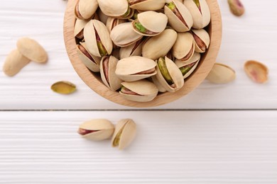 Tasty pistachios in bowl on white wooden table, top view. Space for text