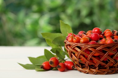 Photo of Ripe rose hip berries with green leaves on white wooden table outdoors. Space for text