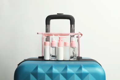 Photo of Cosmetic travel kit in plastic bag on suitcase against light background