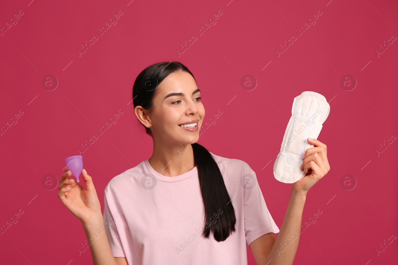 Photo of Young woman with menstrual cup and pad on bright pink background