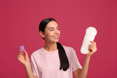 Young woman with menstrual cup and pad on bright pink background