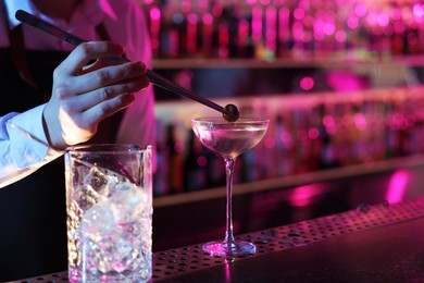 Photo of Bartender adding olive into Martini cocktail at bar counter, closeup. Space for text