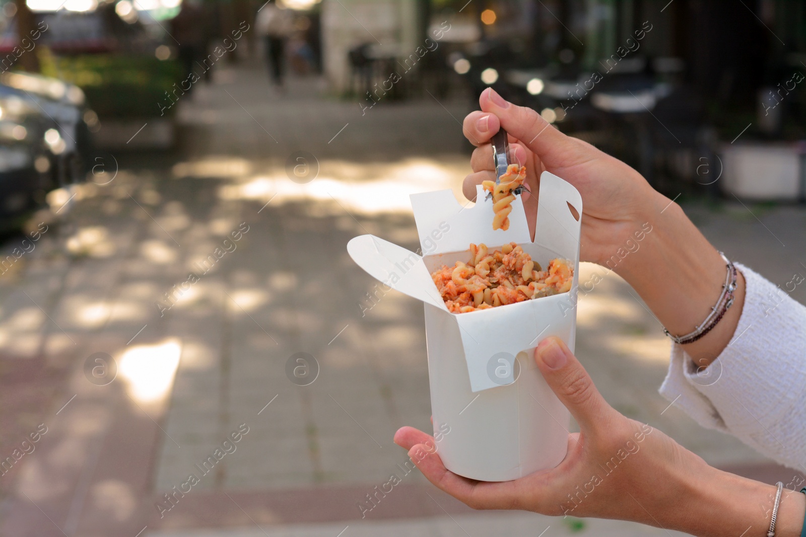 Photo of Woman eating takeaway noodles from paper box with fork outdoors, closeup and space for text. Street food