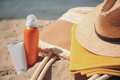Sunscreens, straw hat, bag and towel on beach, closeup. Sun protection care