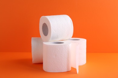 Photo of Soft toilet paper rolls on orange background, closeup