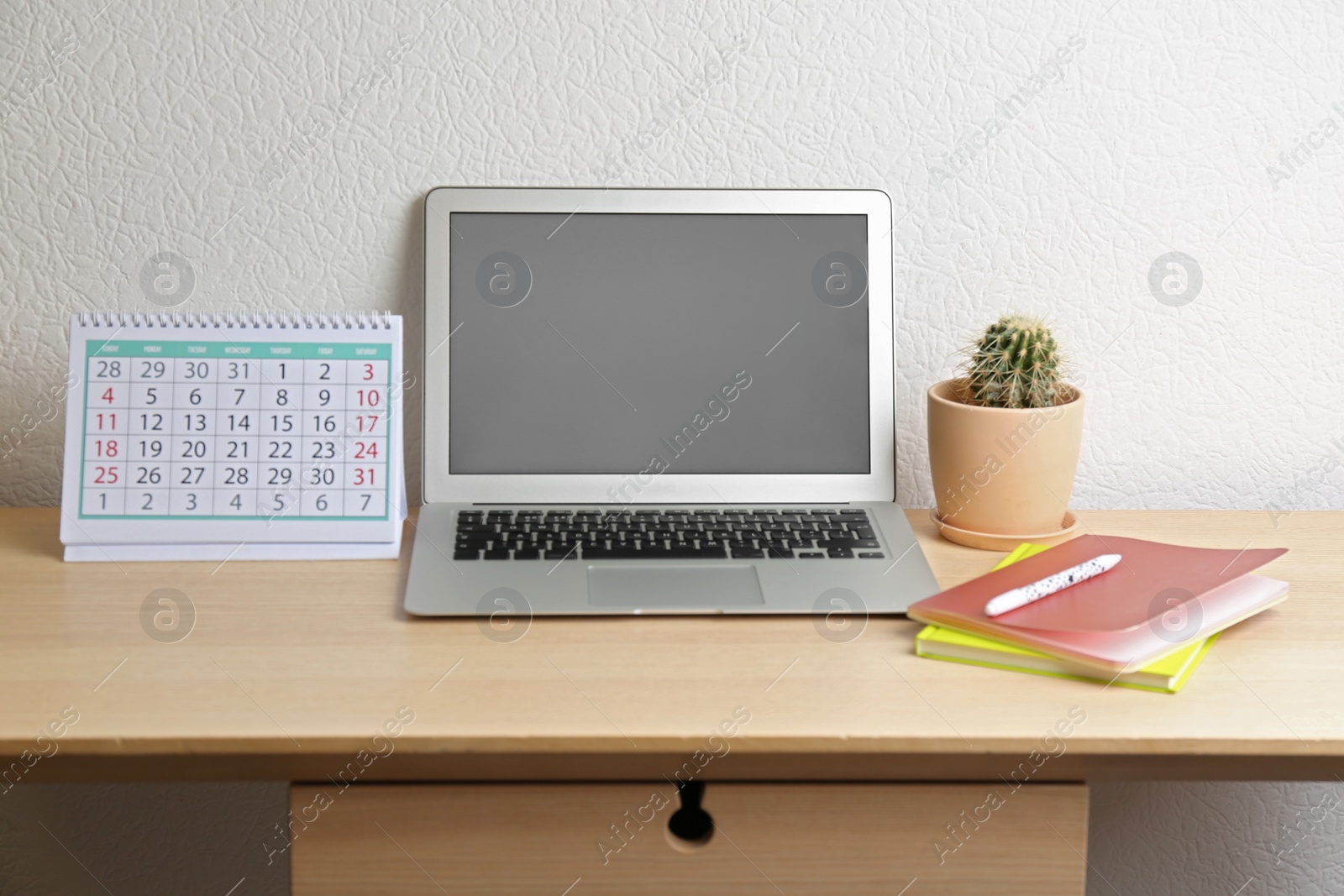 Photo of Paper calendar and laptop with blank screen on wooden table near white wall. Space for design