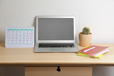 Paper calendar and laptop with blank screen on wooden table near white wall. Space for design