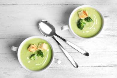 Photo of Delicious broccoli cream soup with croutons served on white wooden table, flat lay