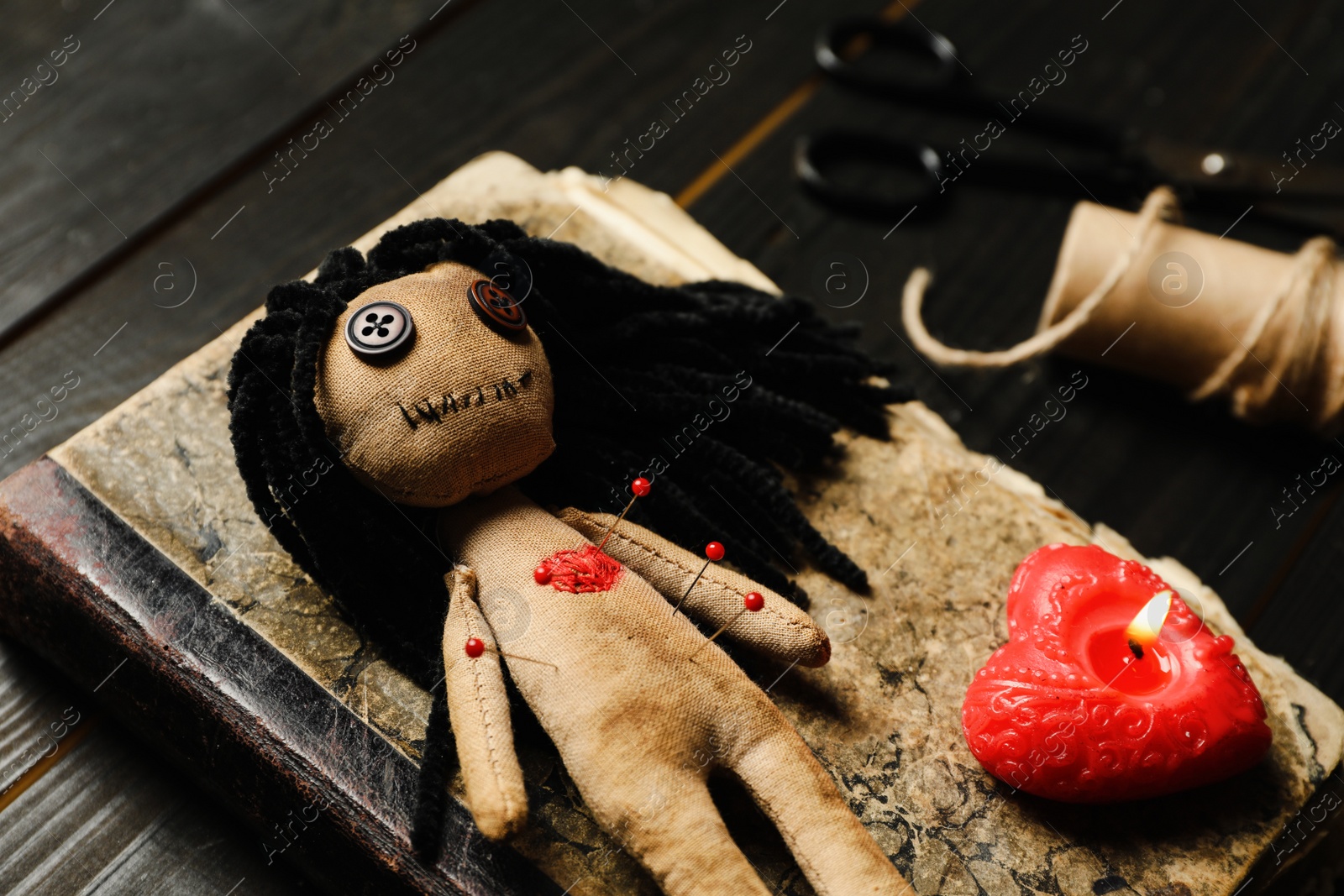 Photo of Voodoo doll with pins, book and heart shaped candle on wooden table, closeup