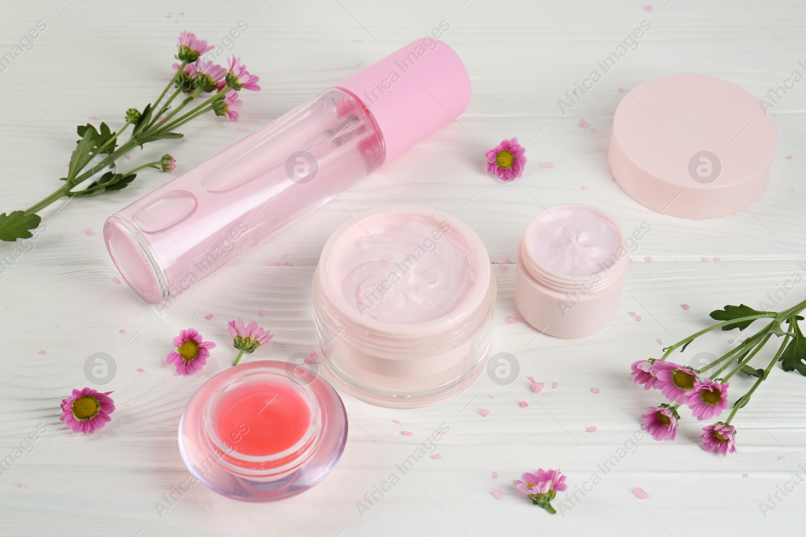 Photo of Homemade cosmetic products and beautiful flowers on white wooden table