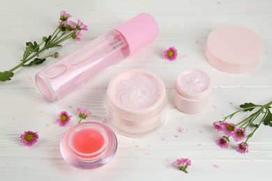 Homemade cosmetic products and beautiful flowers on white wooden table