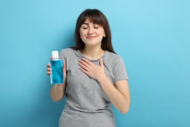 Young woman with mouthwash on light blue background