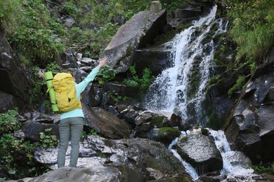 Tourist with backpack near waterfall in mountains, back view. Space for text
