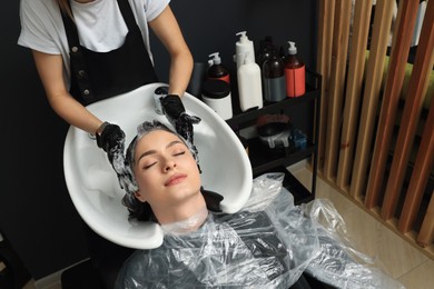Photo of Hairdresser rinsing out dye from woman's hair in beauty salon, above view