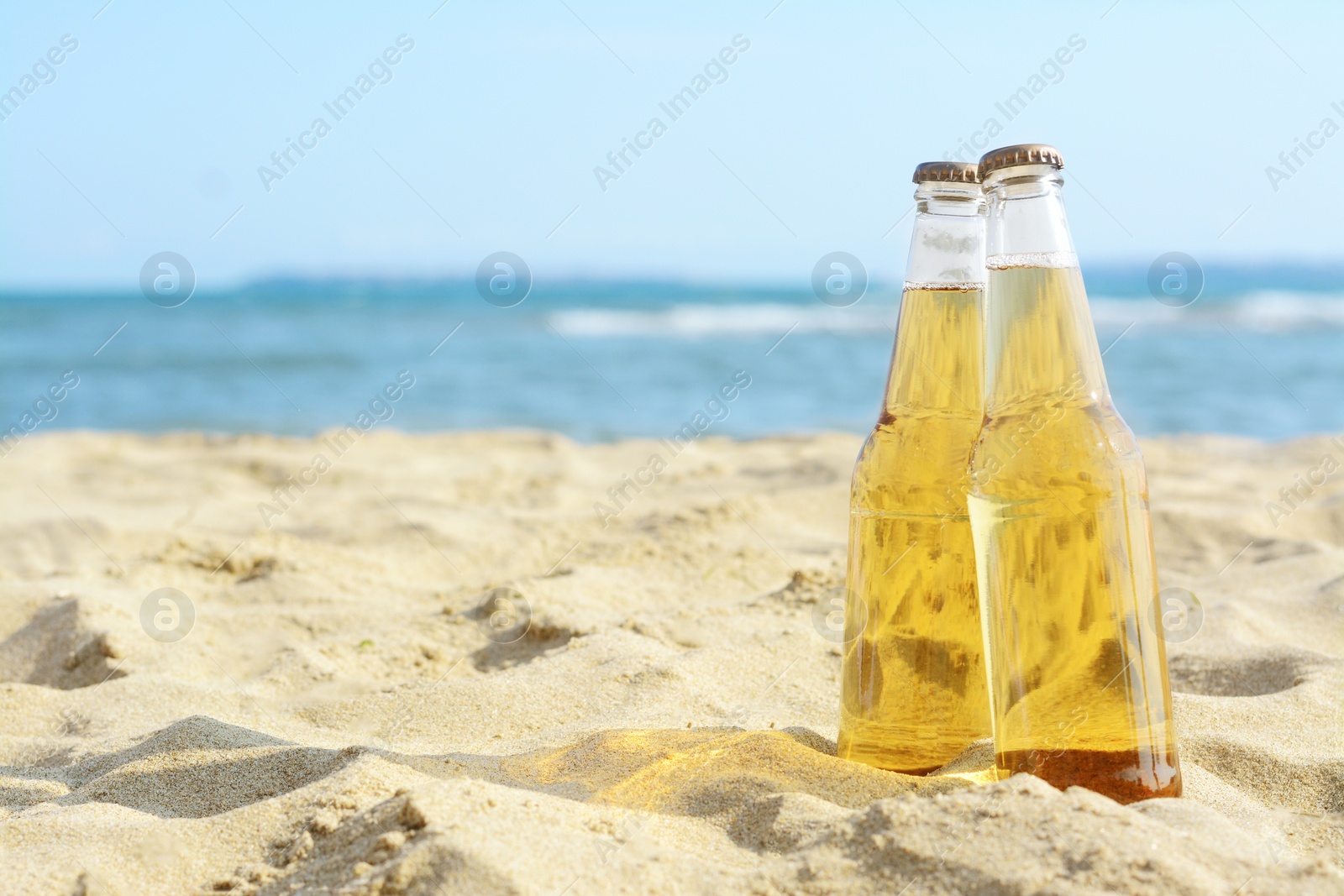 Photo of Bottles of cold beer on sandy beach near sea, space for text