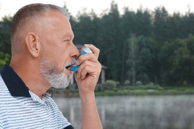 Image of Mature man using asthma inhaler near forest. Emergency first aid during outdoor recreation