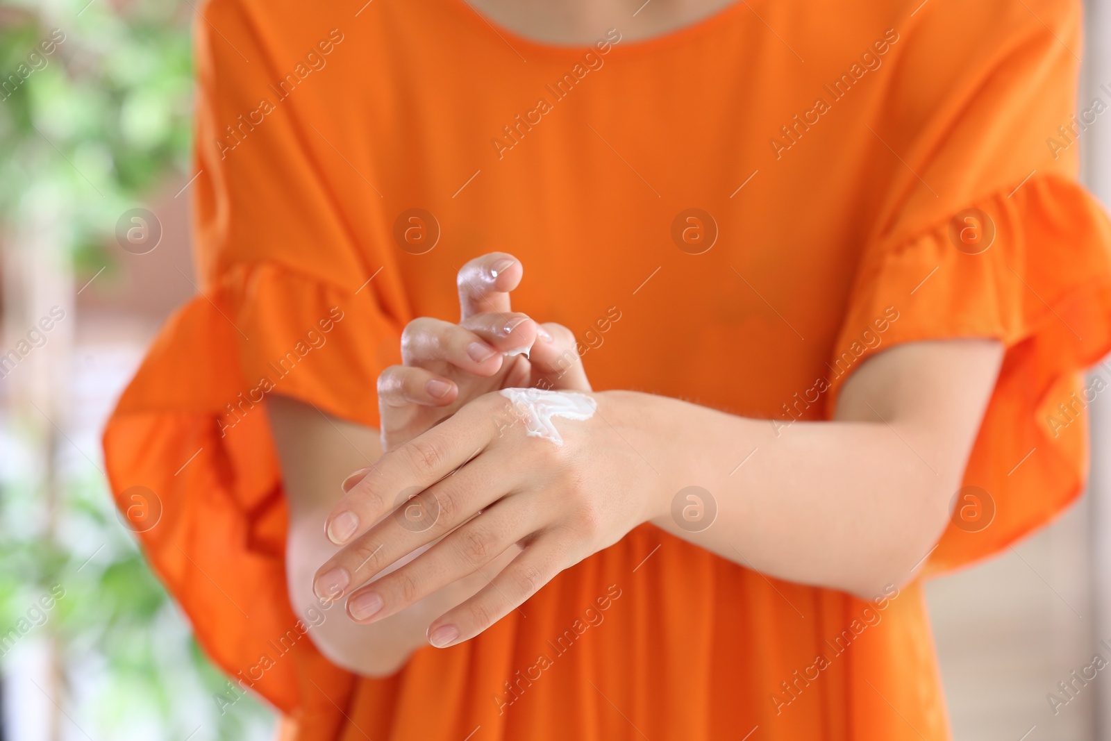 Photo of Young woman applying cream on her hands indoors, closeup