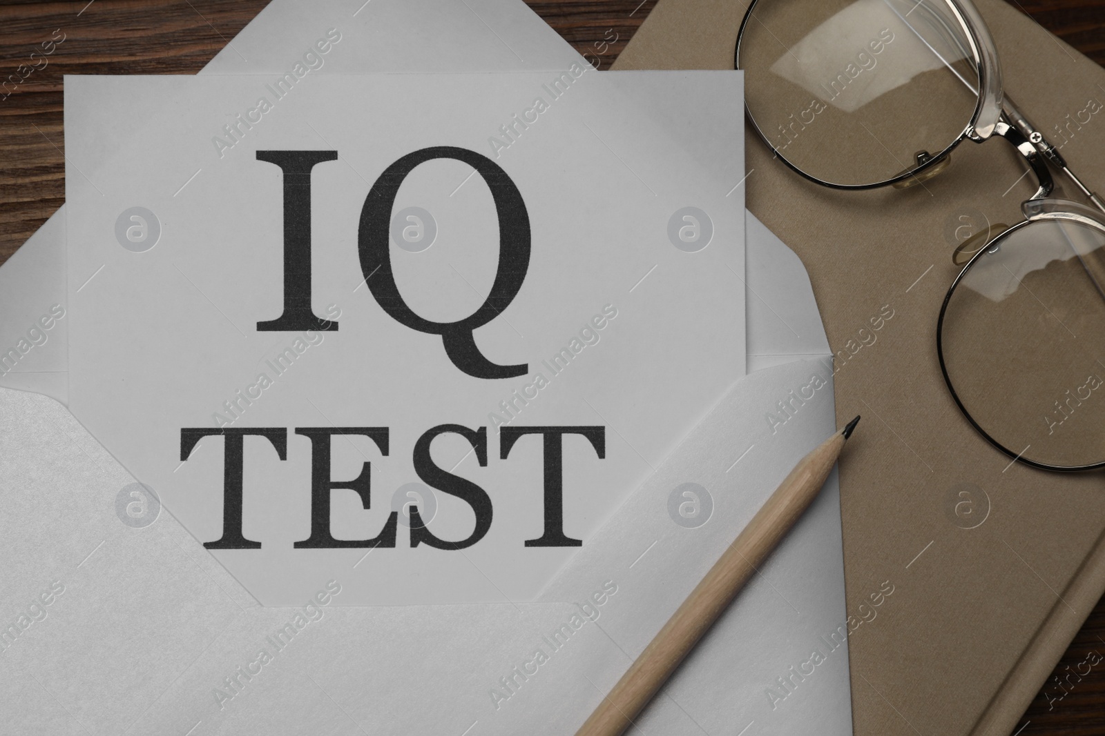 Photo of Paper with words IQ Test in envelope, pencil, notebook and glasses on wooden table, flat lay