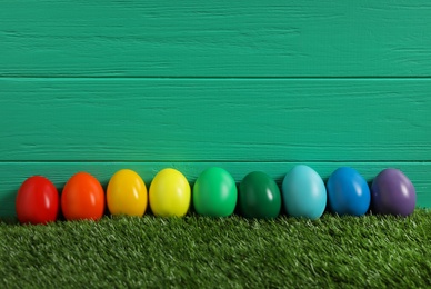 Photo of Bright Easter eggs with on green grass against wooden background