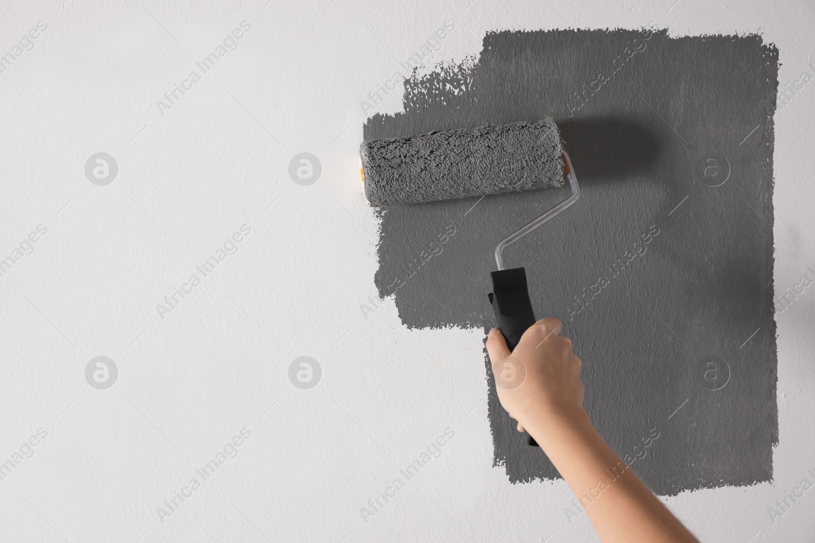 Photo of Woman painting white wall with grey dye, closeup. Space for text