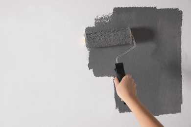 Photo of Woman painting white wall with grey dye, closeup. Space for text