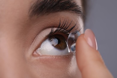 Photo of Closeup view of young woman putting in contact lens on grey background