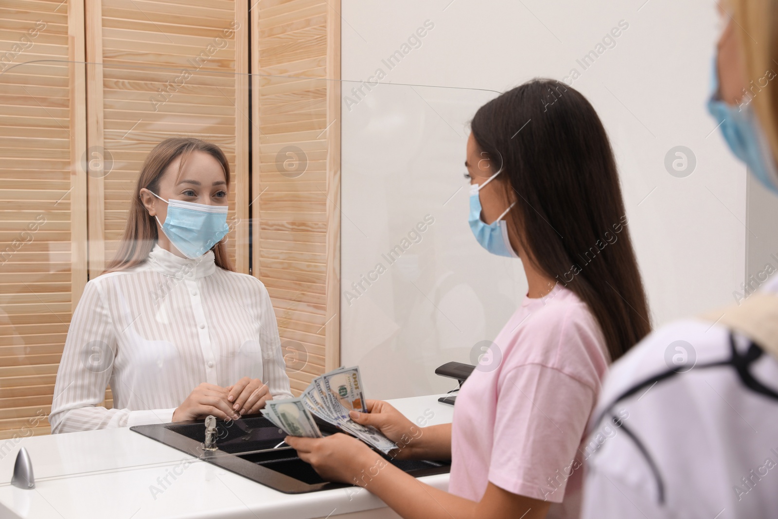 Photo of Woman with protective mask counting money at cash department window in bank. Currency exchange