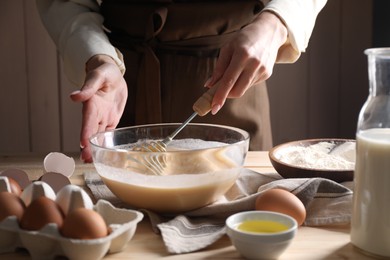 Woman making dough with whisk in bowl at table, closeup