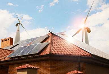 Image of Wind turbines near house with installed solar panels on roof. Alternative energy source