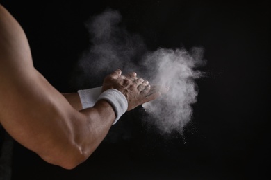 Photo of Young man applying chalk powder on hands against dark background