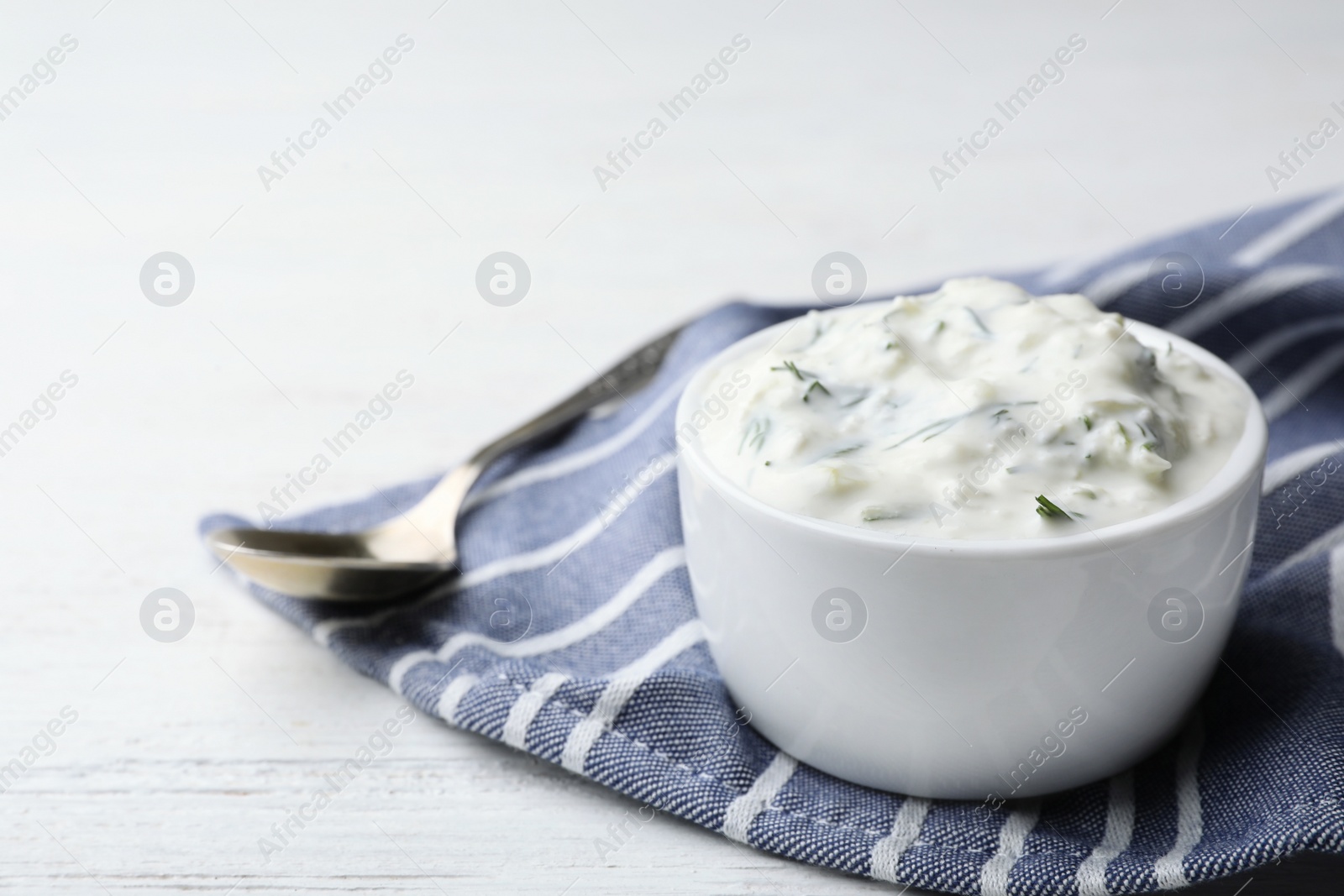 Photo of Cucumber sauce in ceramic bowl and spoon on wooden background, space for text. Traditional Tzatziki