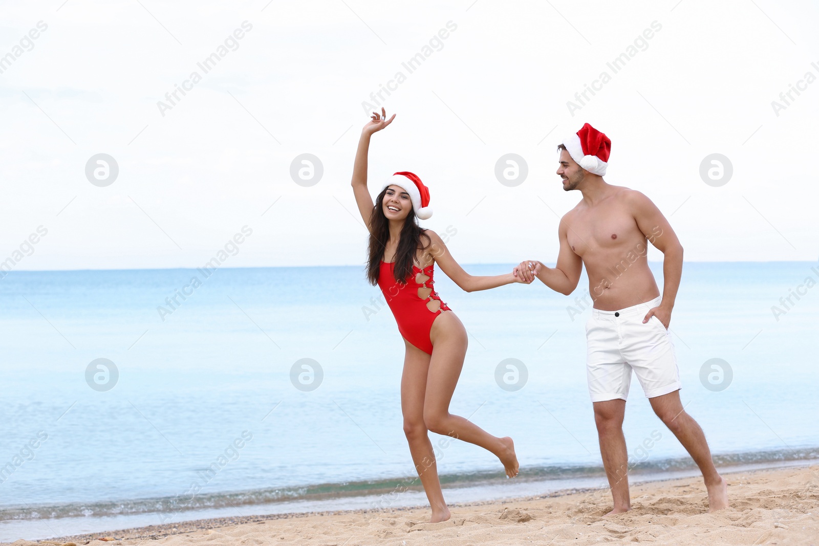 Photo of Happy young couple with Santa hats on beach near sea