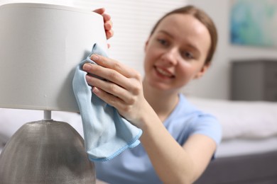 Photo of Woman with microfiber cloth cleaning lamp in bedroom, selective focus