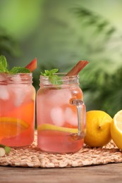 Photo of Mason jars of tasty rhubarb cocktail with lemon fruits on wooden table outdoors