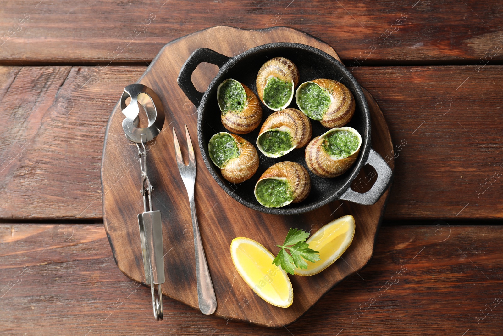 Photo of Delicious cooked snails in baking dish served on wooden table, flat lay