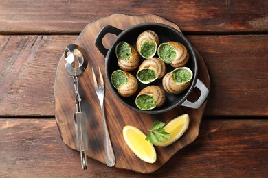 Delicious cooked snails in baking dish served on wooden table, flat lay