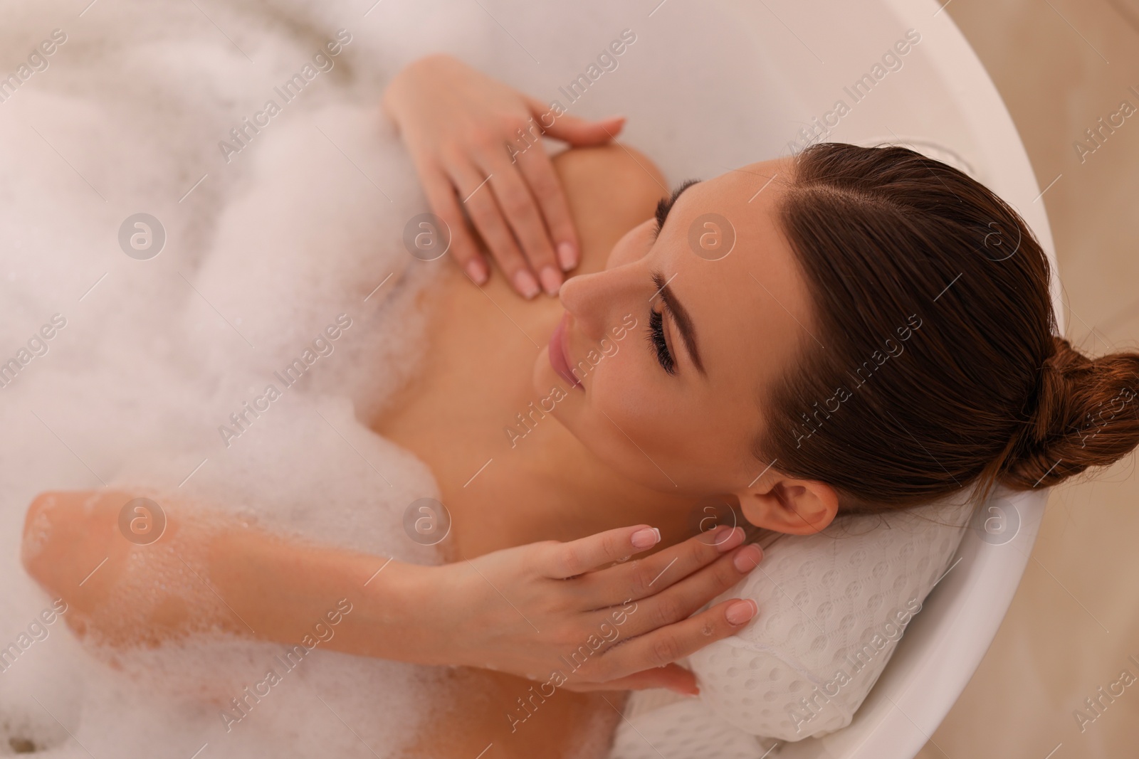 Photo of Young woman using pillow while enjoying bubble bath indoors, above view