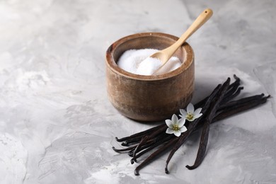 Photo of Vanilla pods, flowers and bowl with sugar on light textured table, closeup. Space for text