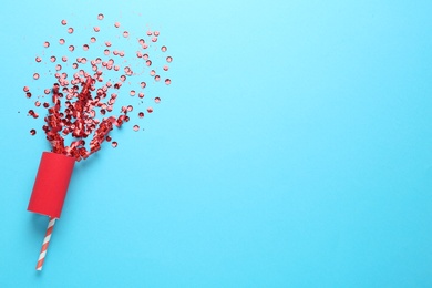 Red confetti and party cracker on light blue background, top view. Space for text