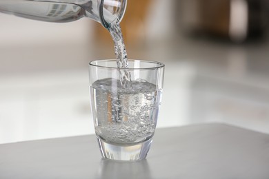 Photo of Pouring water from bottle into glass on light grey marble table in kitchen. Space for text