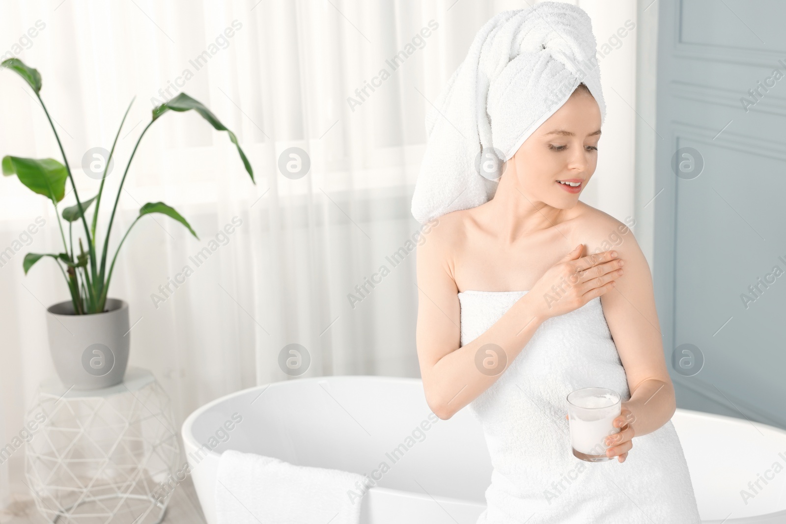Photo of Beautiful young woman applying body cream onto shoulder in bathroom