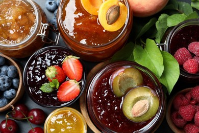Photo of Jars with different jams and fresh fruits on table, flat lay