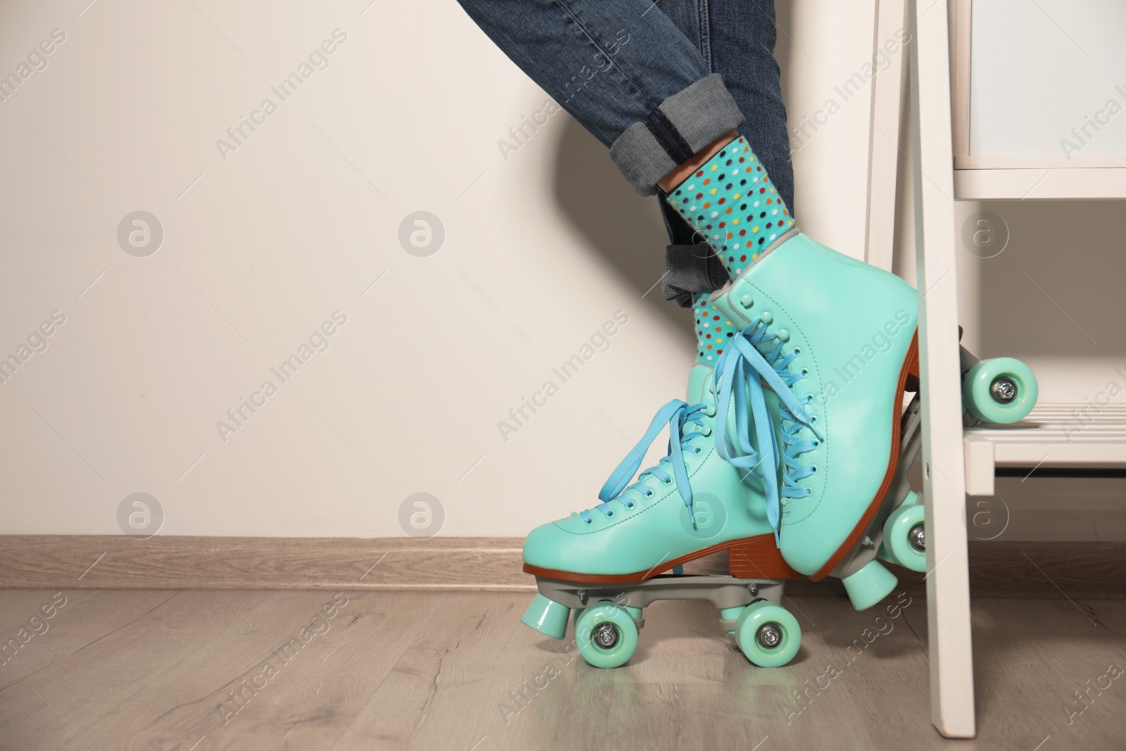 Photo of Young woman with retro roller skates against light wall, closeup. Space for text