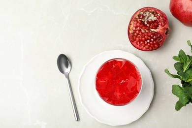 Flat lay composition with red jelly in bowl and pomegranate on light table. Space for text