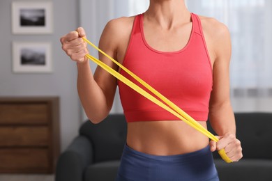 Photo of Woman doing exercise with fitness elastic band at home, closeup