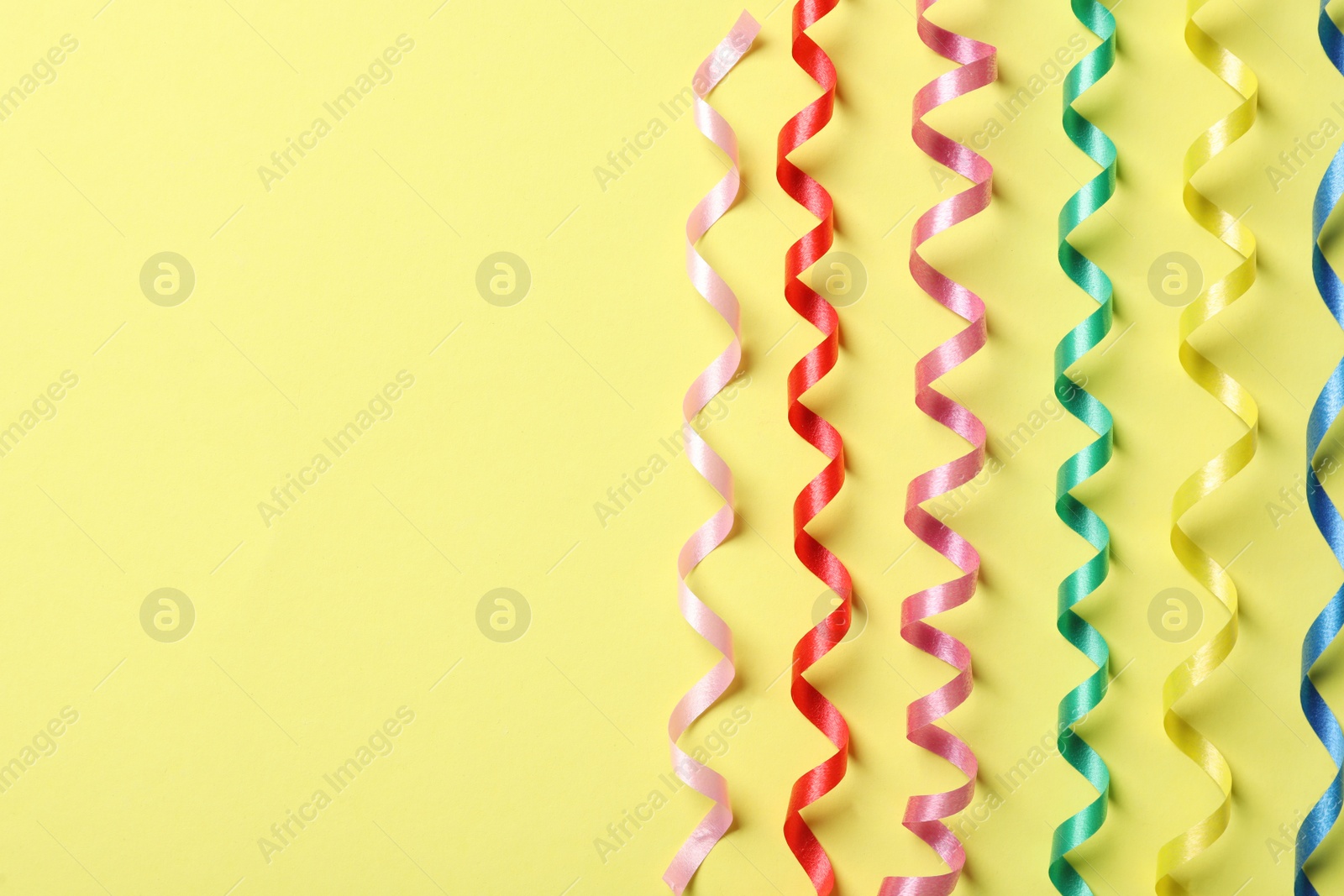 Photo of Colorful serpentine streamers on yellow background, flat lay. Space for text